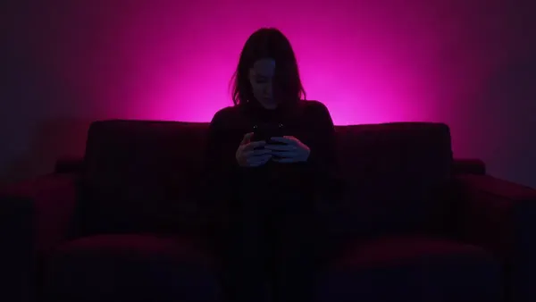 Silhueta de costas num sofá segurando um celular, num quarto escuro com brilho magenta, ilustração do artigo “IA sem censura 2026: os chats IA que permitem NSFW”